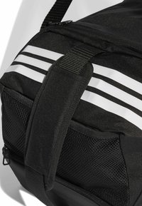 Bolsa deportiva negra con rayas blancas, detalles de malla, tela duradera, cierre con cremallera y correa ajustable para mayor comodidad al transportar.