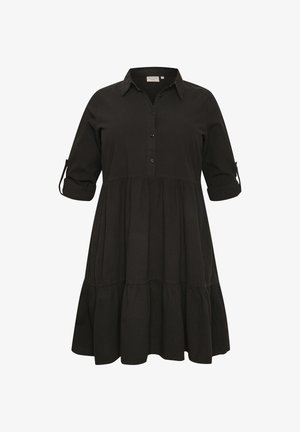 Mustast põlvekõrgusest särk-kleidist, millel on krae, poolpikkade varrukatega, mis on üles keeratud ja nööbitud, kihiline seelik ja ees olev nööpide rida.