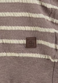 Tela de rayas marrón y beige tejida, con un pequeño parche rectangular marrón etiquetado "KEY LARGO" y un logotipo circular debajo.