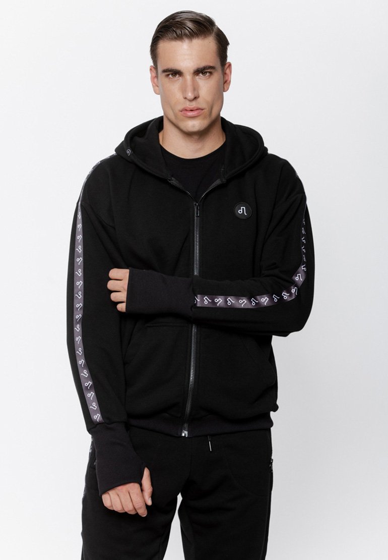 Czarna bluza z kapturem na zamek, wykonana z miękkiego materiału, z dużym kapturem, otworami na kciuki i kontrastującymi wzorzystymi paskami na rękawach.