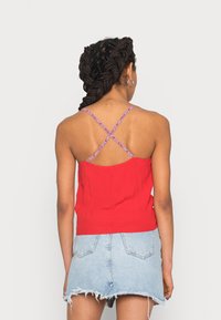 Top sin mangas rojo con tirantes cruzados que cuenta con un detalle estampado; combinado con una falda corta de mezclilla clara con dobladillo deshilachado.