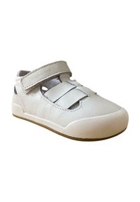Zapato infantil de cuero blanco con una correa de Velcro, puntera redondeada, lados recortados y suela de goma texturizada, diseñado para comodidad y soporte.