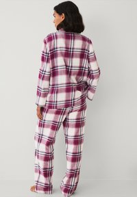 Geruite pyjama's in roze, wit en paars, met een knoopsluiting shirt en losse broek. De stof ziet er zacht en comfortabel uit.