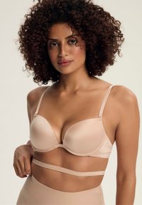 Beżowy biustonosz z wkładkami, z regulowanymi ramiączkami i gładką fakturą. Posiada szeroki pas dolny oraz bezszwowy fason, co zapewnia dopasowany wygląd.