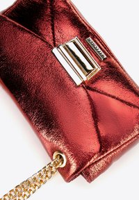 Pochette métallique rouge avec un motif matelassé, quincaillerie dorée et une bandoulière en chaîne. Dispose d'un fermoir rectangulaire et d'une finition texturée.