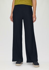 Wijde broek van gestructureerde marineblauwe stof, met een elastische tailleband. Gepaard met donkere sneakers en een groene top.