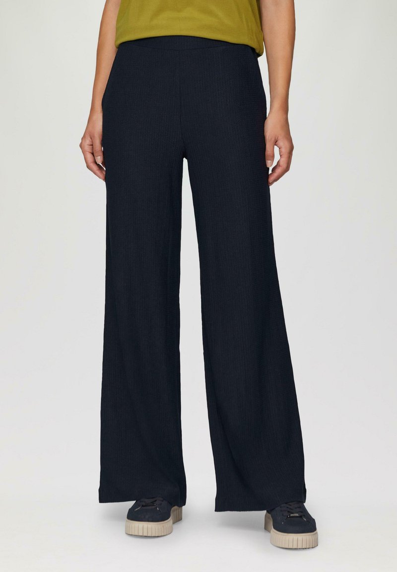 Wijde broek van gestructureerde marineblauwe stof, met een elastische tailleband. Gepaard met donkere sneakers en een groene top.