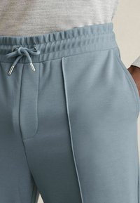 Șorturi de trening bleu deschis, fabricate dintr-un material moale, cu talie elastică, curea de strângere și buzunare laterale. Dispune de detalii subtile cu pliuri.