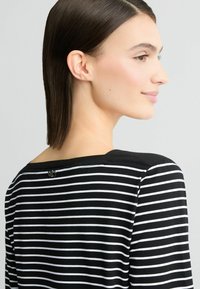 Zwart-wit gestreept shirt met een ronde halslijn, voorzien van een kleine knoopdetail aan de achterkant. Zachte stof en casual lange mouwen.