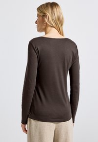 Pitkähihaista ruskeaa puseroa, joka on valmistettu pehmeästä kankaasta. Siinä on pyöreä kaula-aukko ja muotoonommeltu malli. Ei huomattavia kuvioita tai metalliosia näkyvissä.