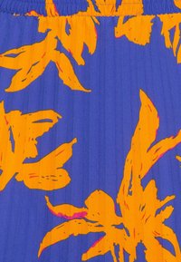 Blommönstrad tyg med livfulla orangea löv mot en blå bakgrund och vertikal ribbtextur. Elastisk midjebanddetalj synlig.