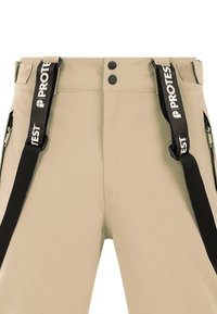 Pantalon beige avec bretelles noires réglables étiquetées "PROTEST" et poches latérales zippées, avec fermeture double bouton à la taille.
