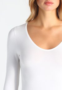 White long-sleeve bodysuit featuring a deep scoop neckline, stretchy fabric, and smooth texture. No visible patterns or hardware details.