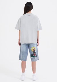 Grijze oversized t-shirt met een zachte textuur, gecombineerd met lichtblauwe denim shorts tot de knie met een wolfgraphic en de tekst 'Born to be Wild'.