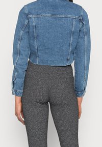 Krótka niebieska kurtka dżinsowa z długimi rękawami, zapinanymi na guziki mankietami oraz widocznymi przeszyciami. Nosi się ją na dopasowane ciemnoszare spodnie o fakturze.