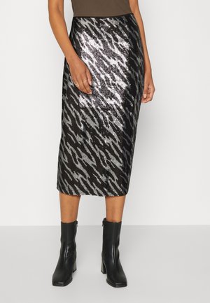 Jupe midi à sequins noirs et argentés avec motif abstrait portée avec des bottines à talons noires et un top marron.