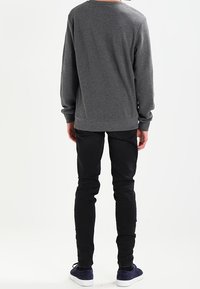 Suéter gris de manga larga con una superficie texturada, combinado con jeans negros ajustados y zapatillas oscuras. El diseño es informal y ajustado.