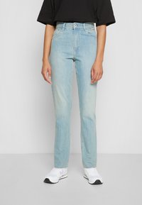 Jeans de cintura alta azul claro com um corte reto, apresentando fecho de botão frontal e desvanecimento subtil. Combinados com ténis brancos.