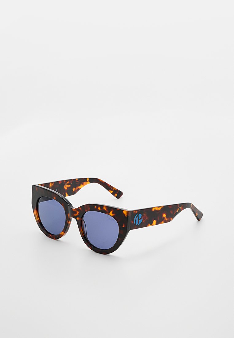 Schildpatt-Katze-Augen-Sonnenbrille mit dunkelblauen Gläsern und einem kleinen blauen Logo auf dem rechten Bügel, auf einem weißen Hintergrund präsentiert.
