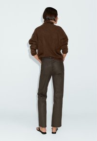 Brown oversized sweater with a high collar, paired with dark brown straight-leg jeans and black flat sandals. Simple, textured materials visible.