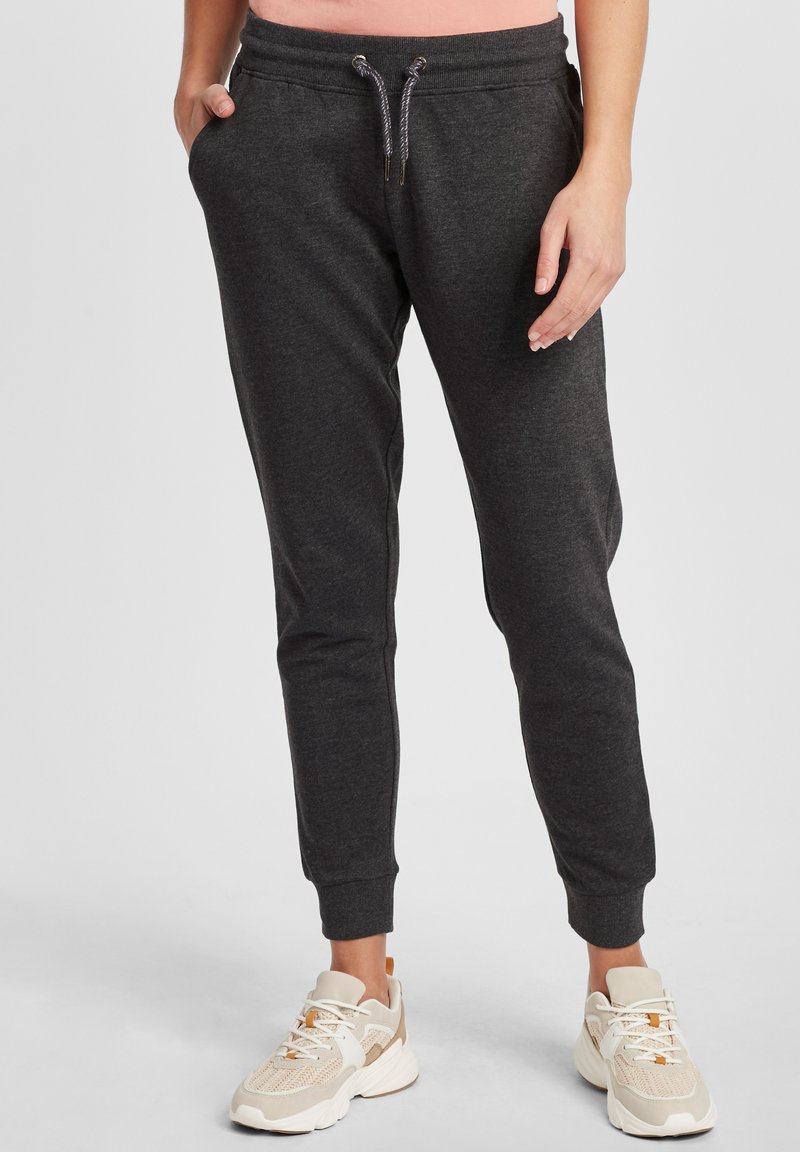 Dunkelgraue Jogginghosen mit elastischem Bund, Kordelzug, seitlichen Taschen und schmalen Bündchen, kombiniert mit hellen Sneakers.