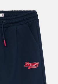 Calças de jogging azul marinho com cintura elástica e cordão apresentam um logótipo bordado vermelho com a inscrição "Tommy" e "CLASSE DE 1985".