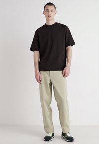Black cotton t-shirt with a relaxed fit paired with light khaki trousers. Model wears green and white sneakers. Minimalist design.