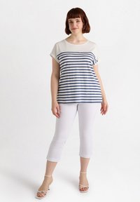 Camiseta de rayas azul marino y blanca con mangas cortas y escote redondo, combinada con pantalones blancos recortados y tacones con tiras.