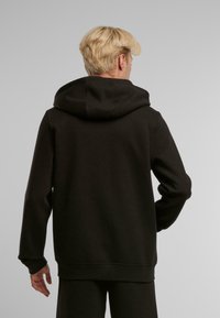 Sudadera negra con una gran capucha, puños y cintura acanalados, hecha de tela suave; exhibida desde la parte de atrás con un diseño sencillo.
