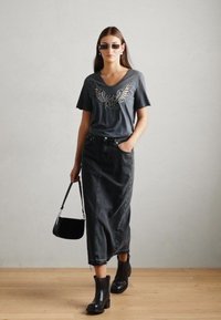 Šedé tričko s grafickým motivem křídel, černá džínová maxi sukně, černé kotníkov�é boty a malá černá kabelka. Hladká textura, ležérní design.
