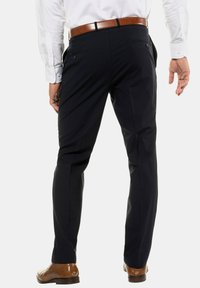 Pantaloni scuri blu navy con una vestibilità su misura, dotati di tasche posteriori e dettaglio delle pieghe. Abbinati a una cintura e scarpe in pelle marrone.