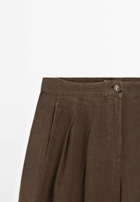 Pantalons en lin marron avec un devant plat, des plis et une fermeture à bouton unique à la taille. Tissu texturé avec un léger éclat.