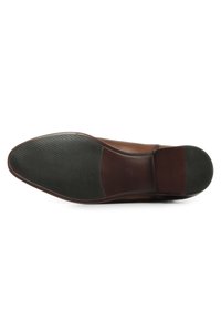 Semelle en cuir marron avec une texture en caoutchouc antidérapant, présentant un bord lisse et une section de talon contrastante en noir.