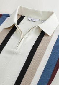 Polo en maille à col avec rayures verticales en noir, beige, bleu et bordeaux, doté d'une fermeture éclair partielle sur le devant.