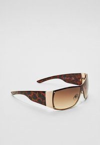Solbriller med skildpadde-ramme, brune gradientlinser, guld detaljer og et dristigt, oversized design til UV-beskyttelse.