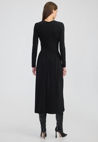 Czarna sukienka z długimi rękawami, dopasowanym korpusem i marszczoną talią, z zapięciem na zamek z tyłu oraz zwiewnym dołem.