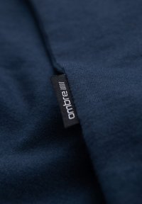 Nærbillede af mørkeblåt stof med et lille sort mærke med teksten "ombre" syet ind i sømmen.