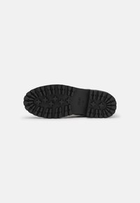 Suela de zapato de goma negra con un patrón de relieve profundo, que presenta estrías texturizadas y agarres en forma de cruz para tracción. Incluye la impresión del logo de la marca.