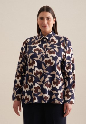 Vloeiende marineblauwe blouse met groot bloemenpatroon in crèmekleur en bordeauxrood. Heeft een puntige kraag en lange mouwen, gemaakt van lichte stof.