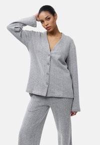 Grijze cardigan van een gestructureerde stof, met een V-hals, lange mouwen en vijf knopen. Gepaard met bijpassende grijze broek.