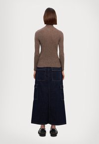 Brown ribbed long-sleeve top paired with a dark blue denim maxi skirt featuring large side pockets and a straight hem. Black shoes complete the look.