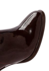 Chaussure à talon haut en cuir verni marron avec une finition brillante, bout arrondi et subtile couture rouge le long du bord.