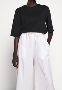 Svart kortärmad t-shirt som kombineras med vida, högmidjade vita byxor med dragsko i midjan. Mjuka, lätta tyger.