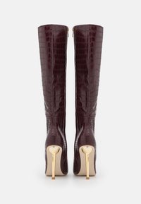 Knee-high burgundy krokodillikuvioiset saappaat, joissa on kiiltävä pinta, korkea kultainen stilettokorko ja vetoketjukiinnitys sivulla.