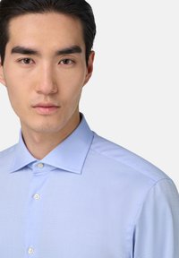 Světle modrá košile s texturovanou tkaninou, zapínání na knoflíky a špičatým límcem. Disponuje jemnými středícími akcenty.