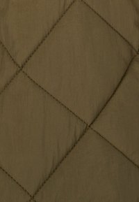Tejido acolchado en verde oliva, con costuras diagonales y una textura suave y ligeramente brillante. Adecuado para prendas de abrigo o ropa de cama.