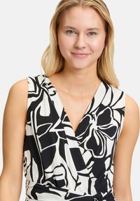 Zwart-witte wikkeljurk met een bloemenpatroon, mouwloos ontwerp, V-halslijn en een gladde stof met een lichte glans.