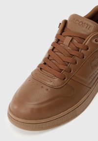 Brązowe skórzane sneakersy o gładkiej teksturze, z okrągłym noskiem, sznurowanym przodem oraz wytłoczonym logo na języku. Delikatne perforacje na nosku.
