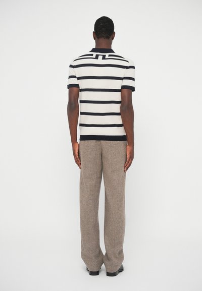 Csíkos kötött pólóing rövid ujjal, krém és tengerészkék színben, barna gyapjú nadrággal párosítva, hátulról bemutatva. Texturált anyag és strukturált fazon.