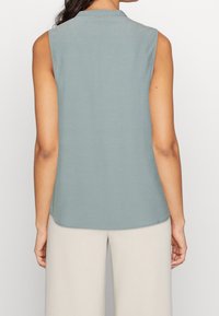 Haut sans manches en bleu-gris doux, avec un col rond et une texture lisse et douce. L'ourlet est légèrement arrondi à l'arrière.